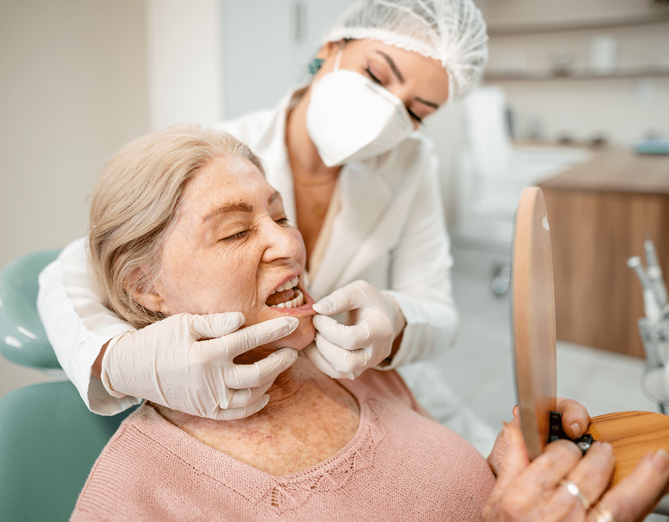 Hygienist adjusting dentures while patient checks mirror